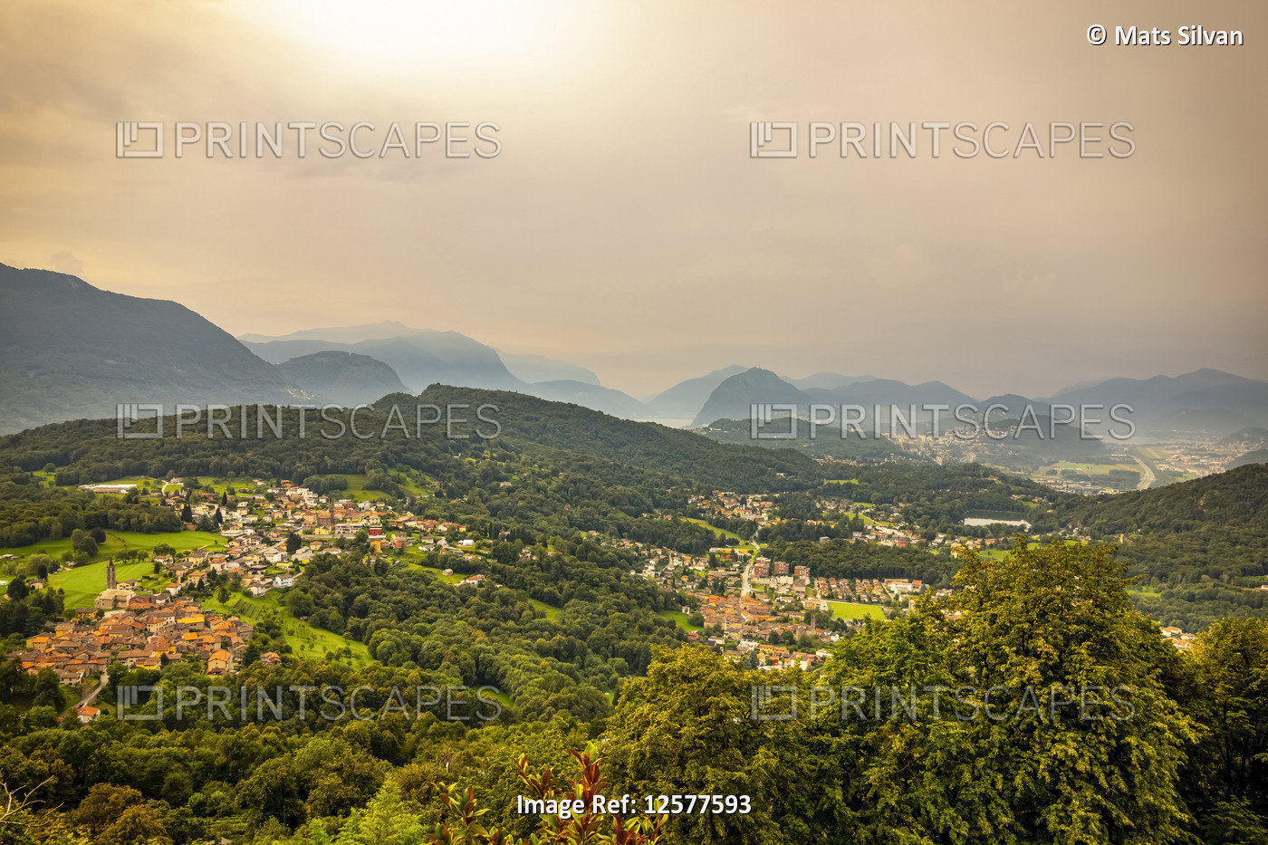 Sunlight glowing through the overcast sky over the rolling hills of Lugano; ...