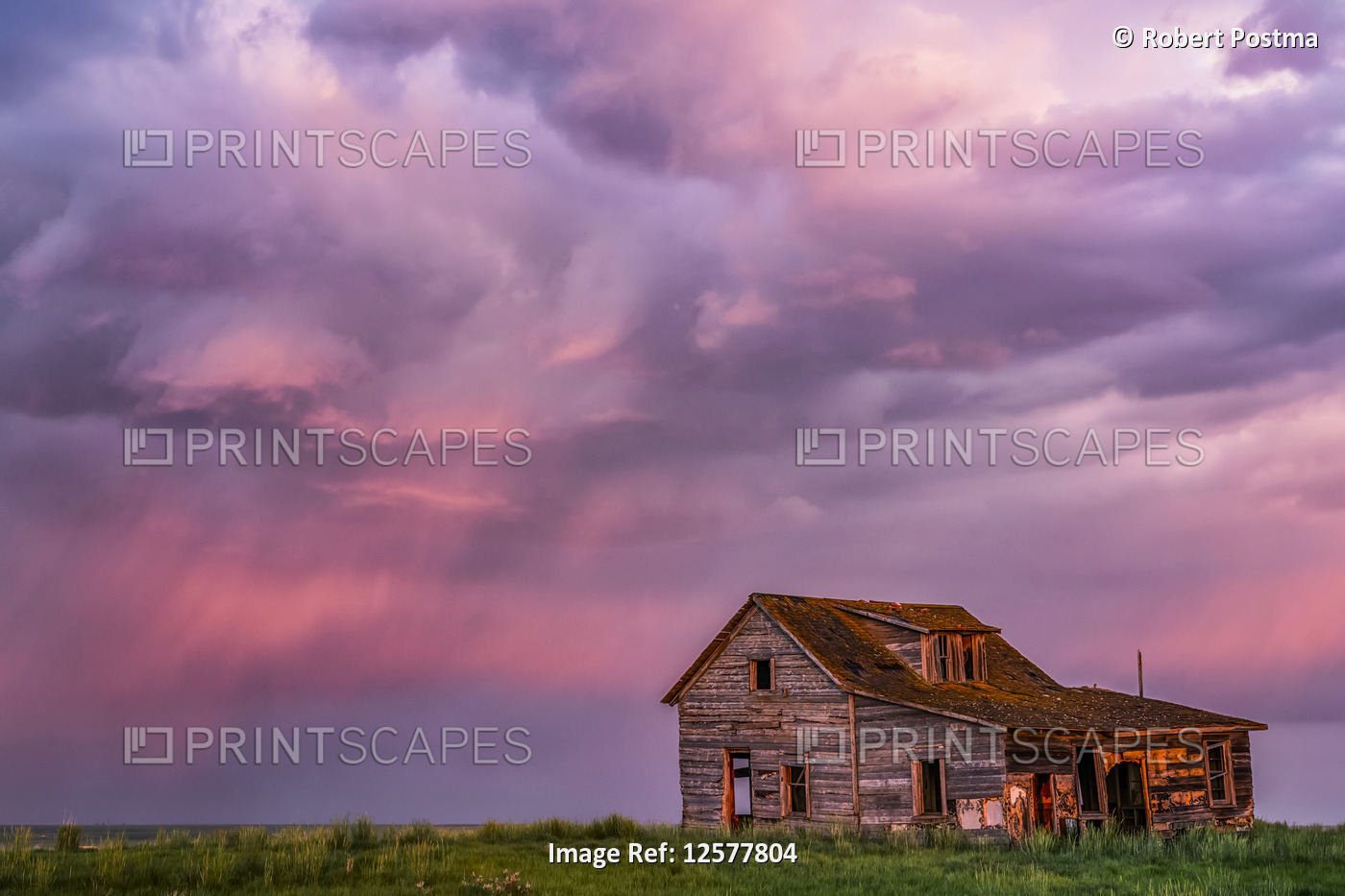 Abandoned barn on farmland with storm clouds glowing pink; Val Marie, ...