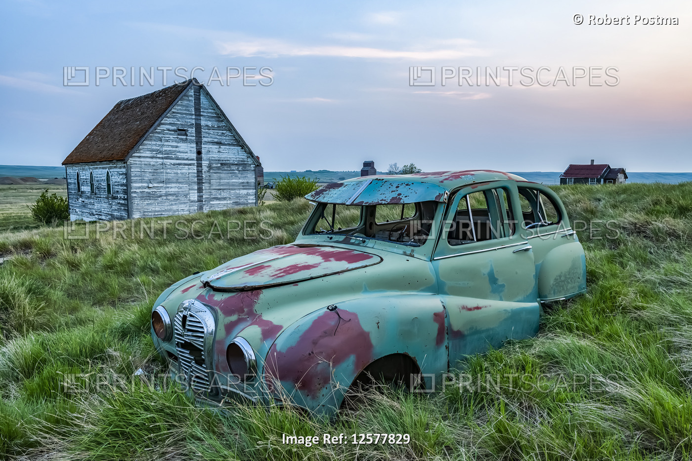Vintage car sitting in the overgrown grass in a field with old buildings on a ...