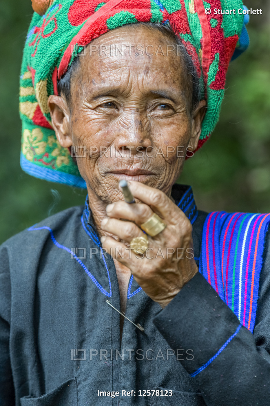Burmese woman wearing a traditional head covering and smoking a cigarette; ...