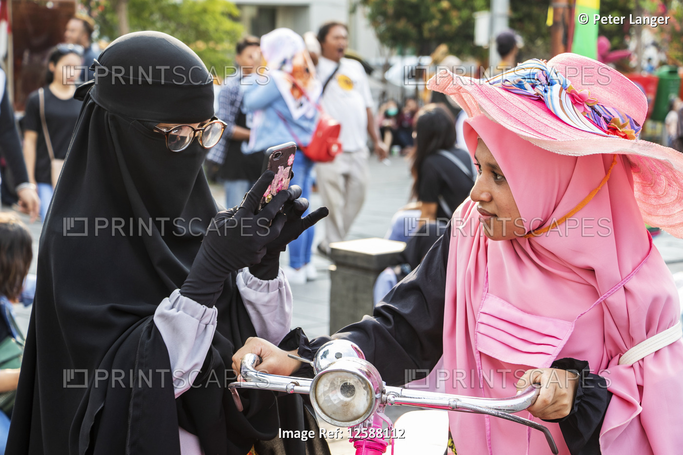 Women on Taman Fatillah square, one using a smart phone and the other on a ...