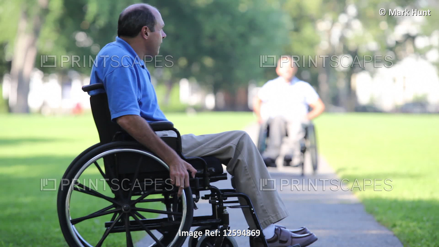 Two men in wheelchairs in a park greeting each other, one with spinal cord ...