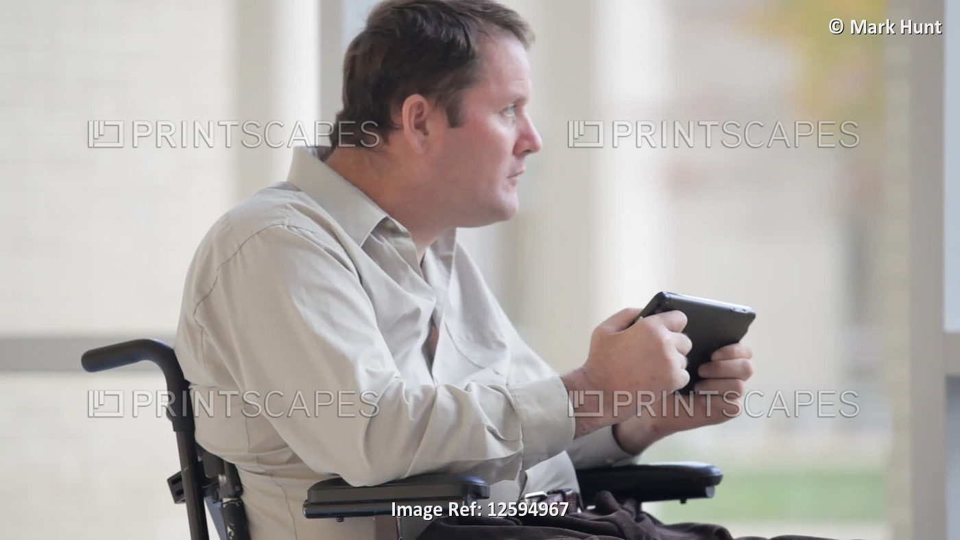Quadriplegic man with spinal cord injury struggling with a tablet in his hands; ...