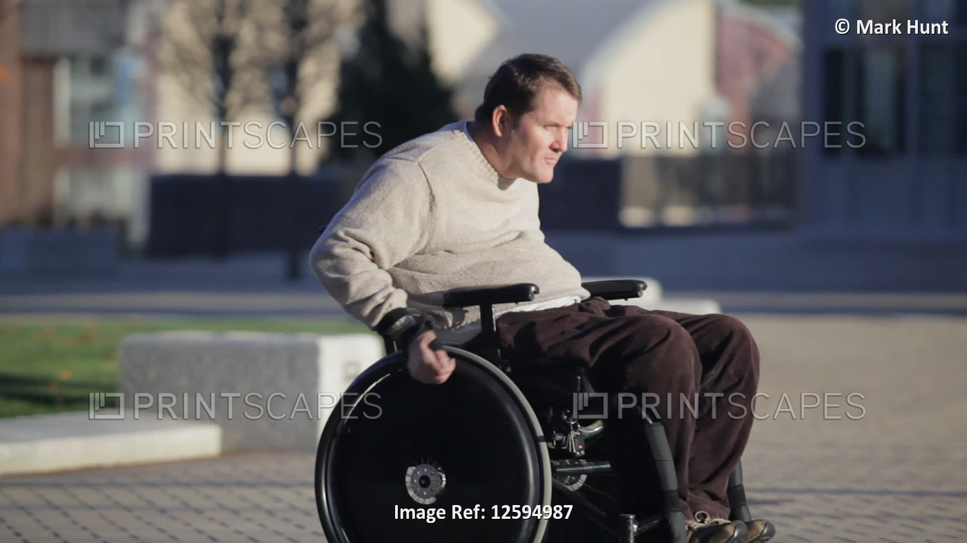 Man with spinal cord injury using wheelchair on campus walkway; United States ...