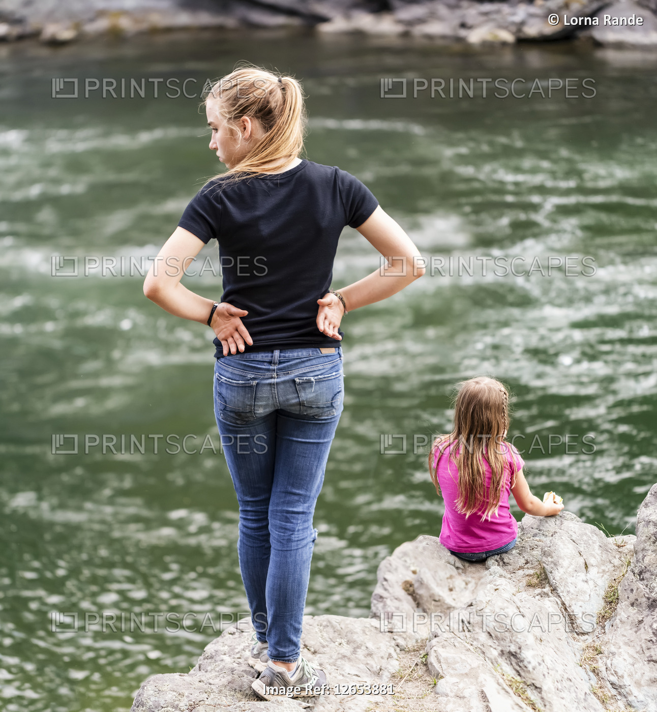 Two sisters spending time together at the edge of a river; British Columbia, ...