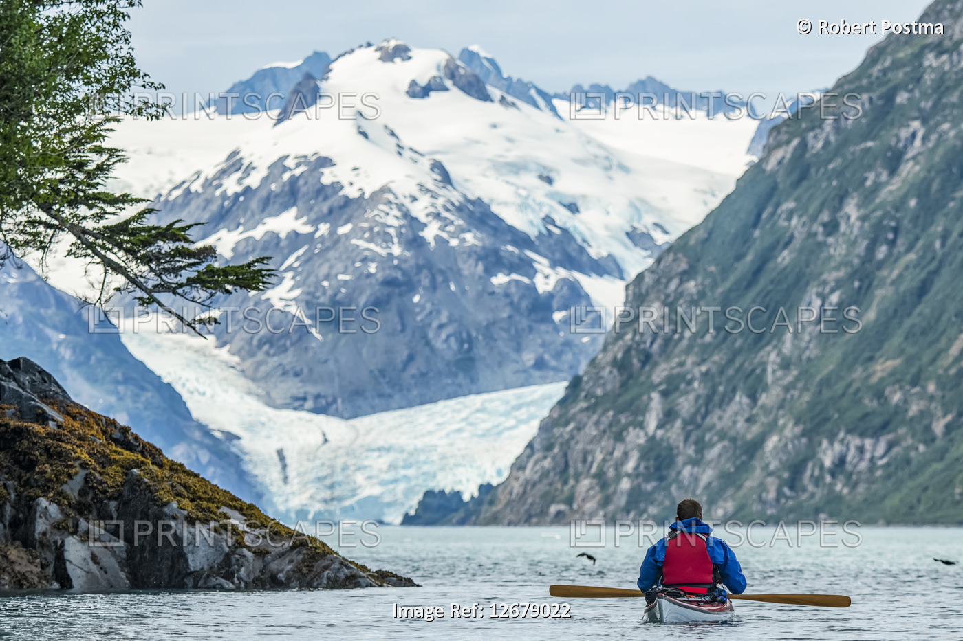 Kayaker paddling in Prince William Sound, Alaska with beautiful mountains in ...