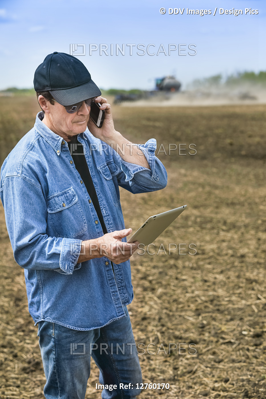 Farmer using a smart phone and tablet while standing on a farm field and ...