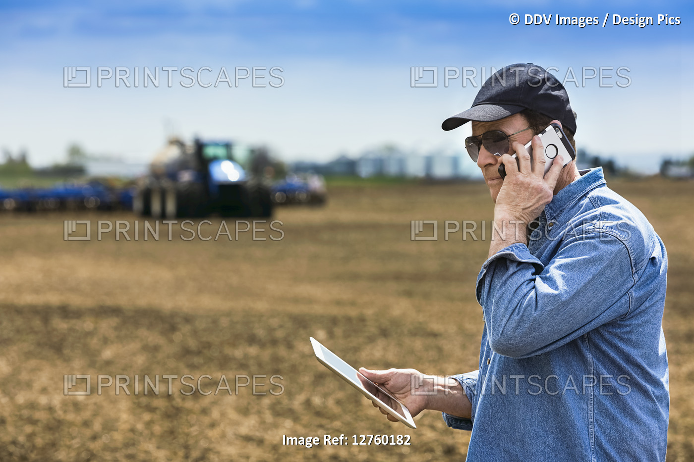 Farmer using a smart phone and tablet while standing on a farm field and ...