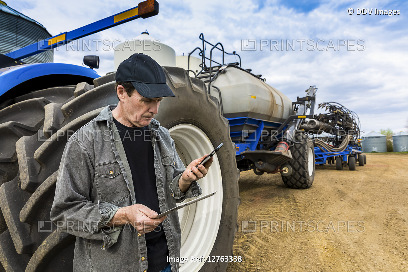 Farmer using a smart phone and tablet while standing on a farm beside ...