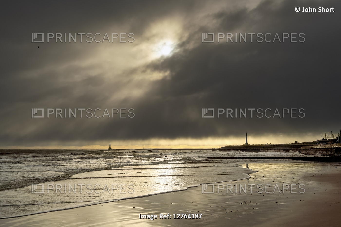 Silhouetted lighthouses along the coastline under dramatic cloudy sky; Whitburn ...