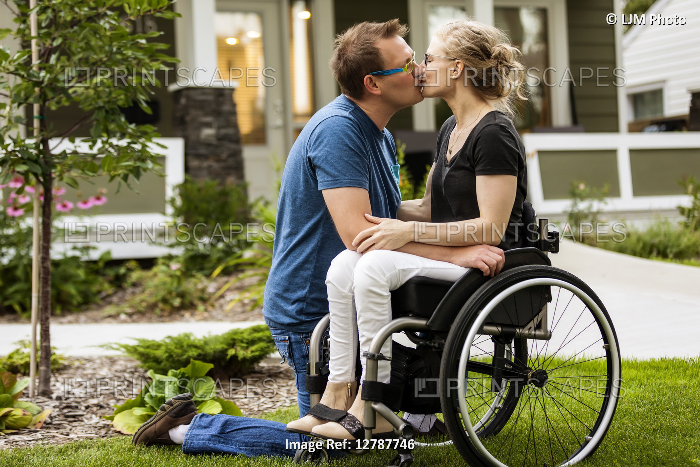 A husband and his paraplegic wife kissing in their front yard on a warm fall ...