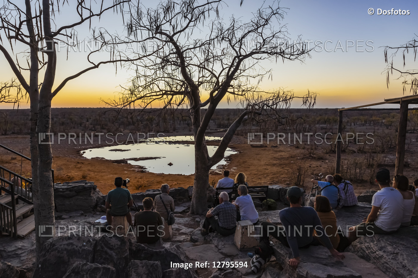 Tourists sit watching for movement around a waterhole at sunset, Etosha ...