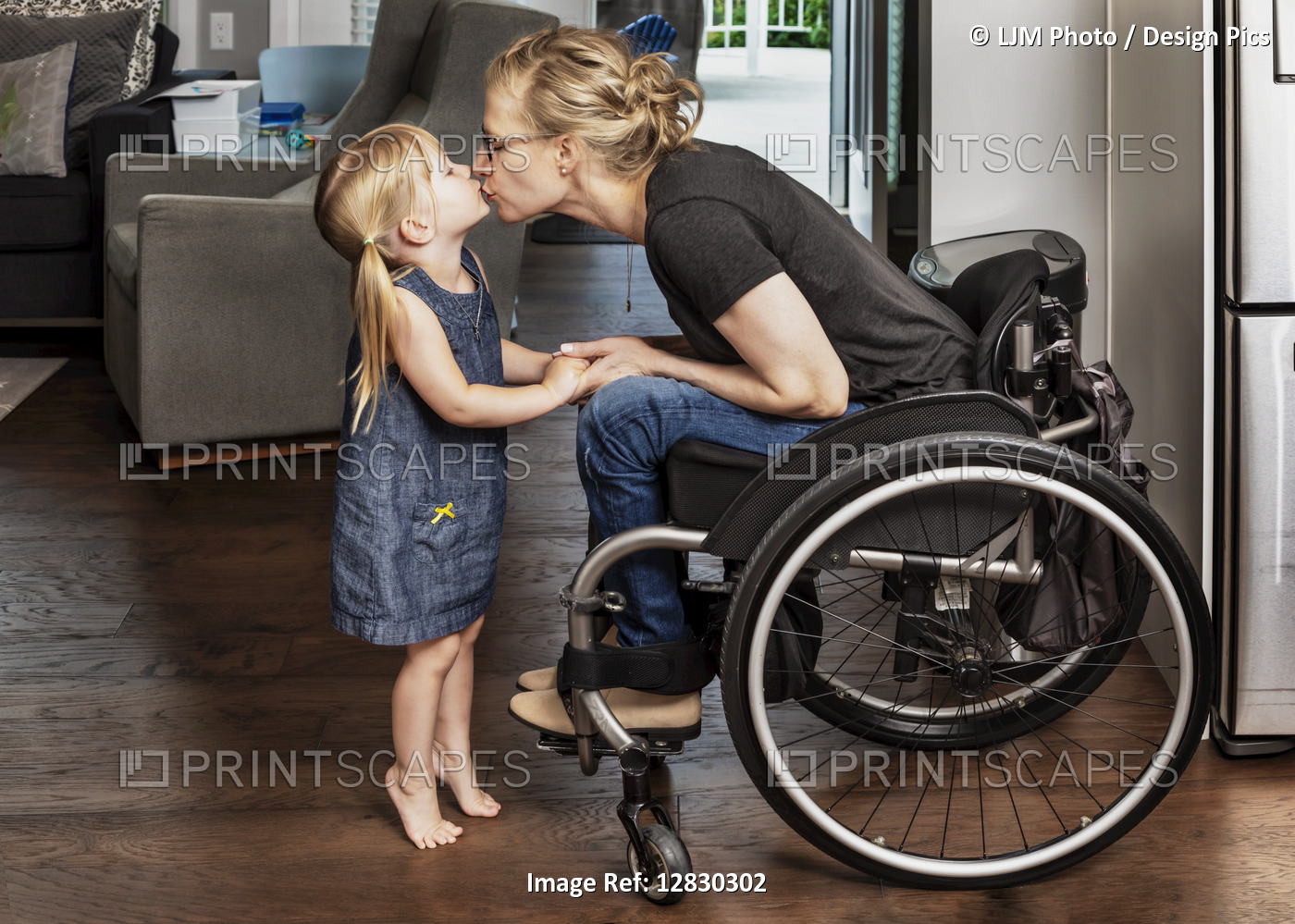 A young girl standing on her tippy-toes to give a kiss to her paraplegic mom ...