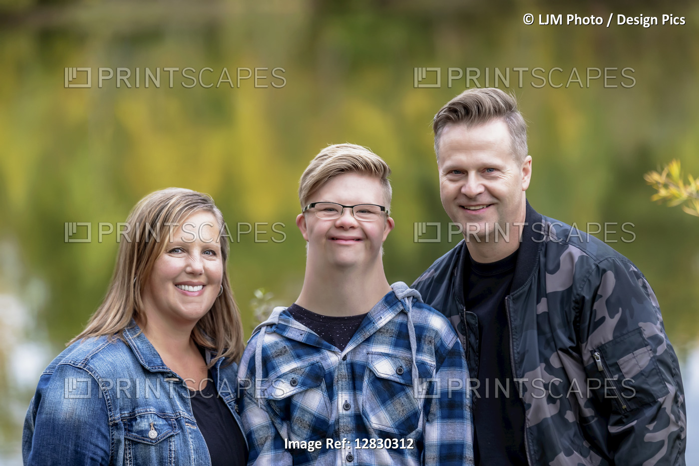 A young man with Down Syndrome posing for a family portrait with his father and ...