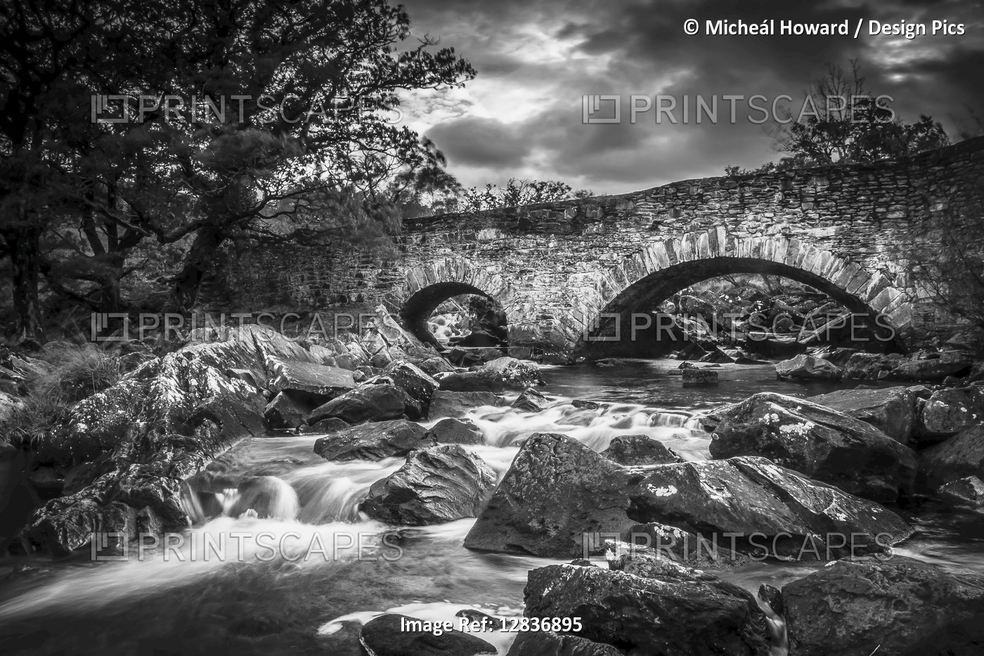 Black and white image of an arched stone bridge over a flowing river; County ...