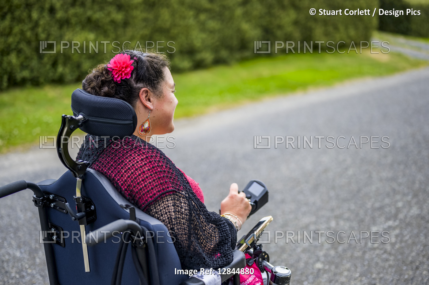 Maori woman with Cerebral Palsy in a wheelchair going down a sidewalk; ...