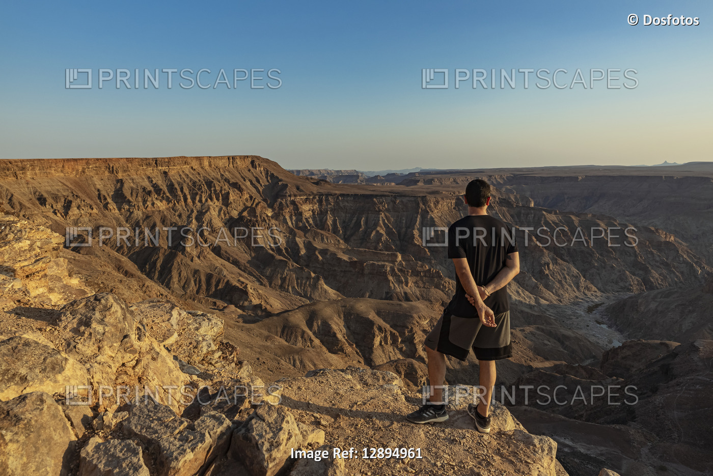 Male tourist stands on a rock ridge overlooking Fish River Canyon; Namibia