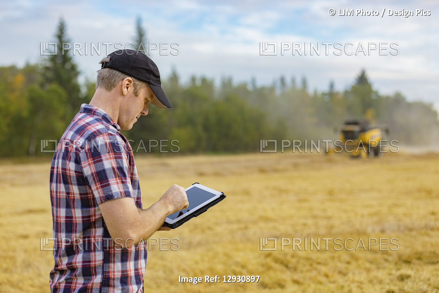 A farmer using his tablet to help manage the wheat harvest while a combine is ...