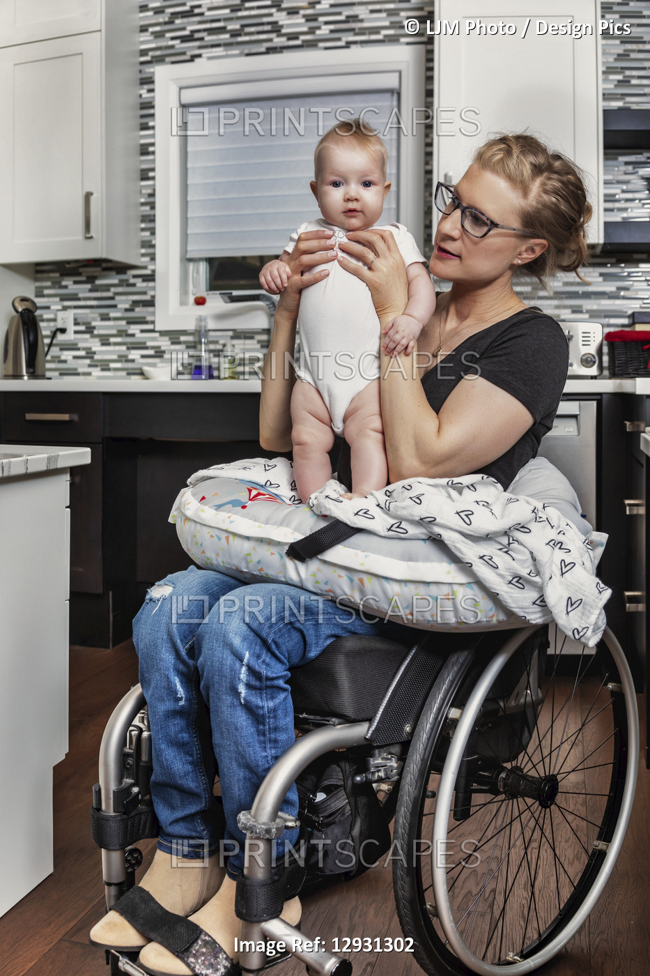 A paraplegic mother holding her baby on her lap, in her kitchen, while sitting ...