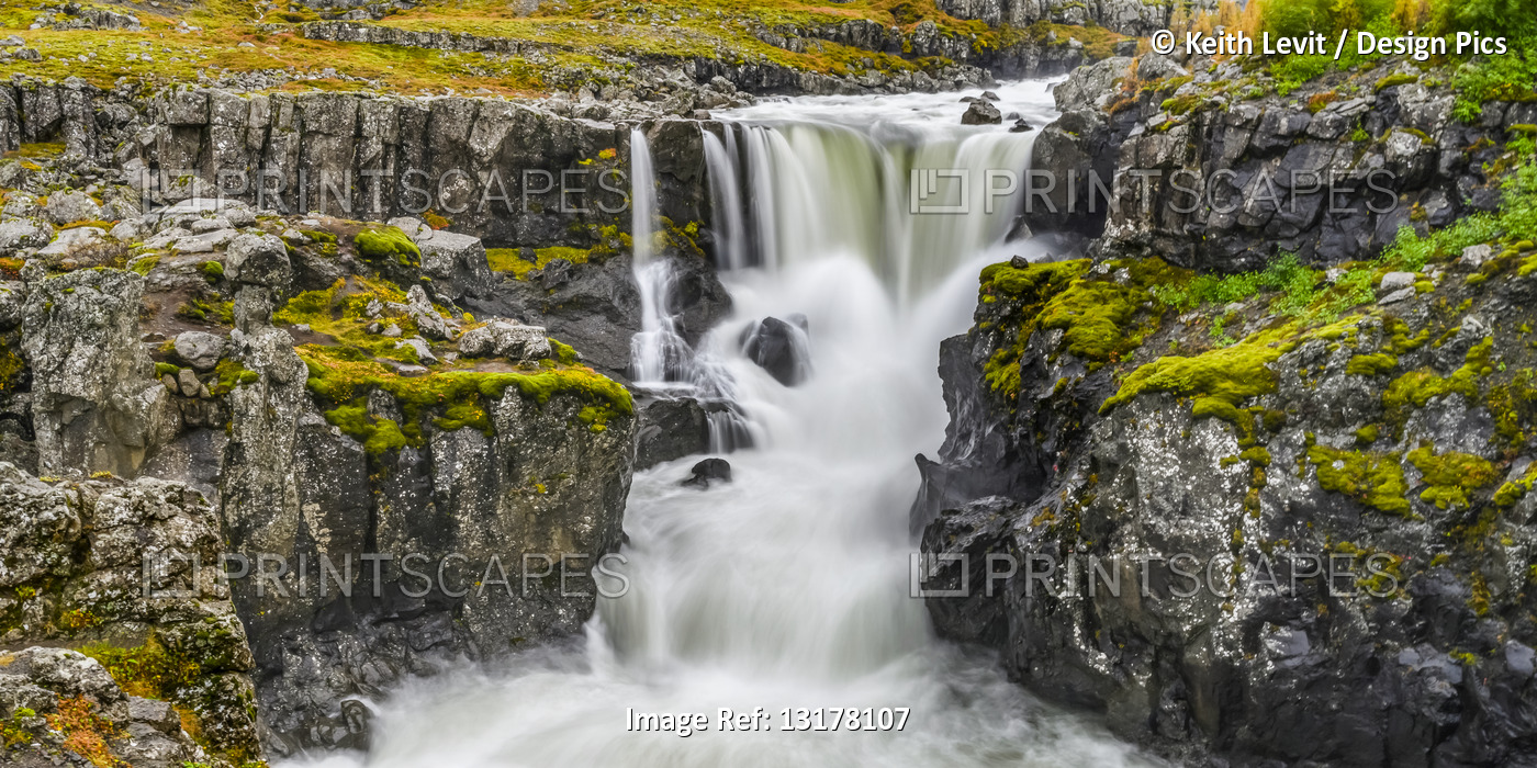 Waterfall and rushing river on a rugged landscape in Eastern Iceland; ...