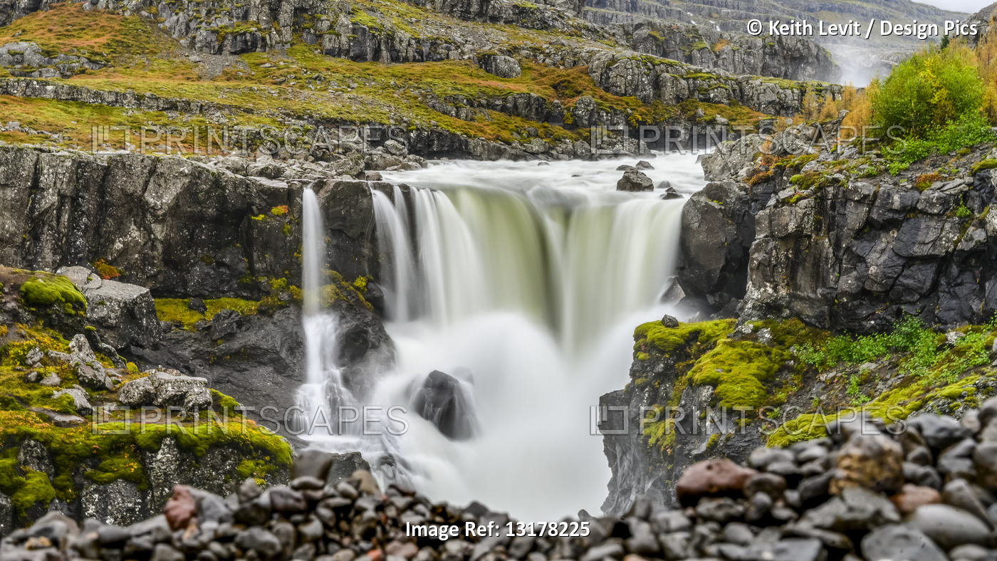 A waterfall over a rocky landscape in autumn colours; Djupivogur, Eastern ...
