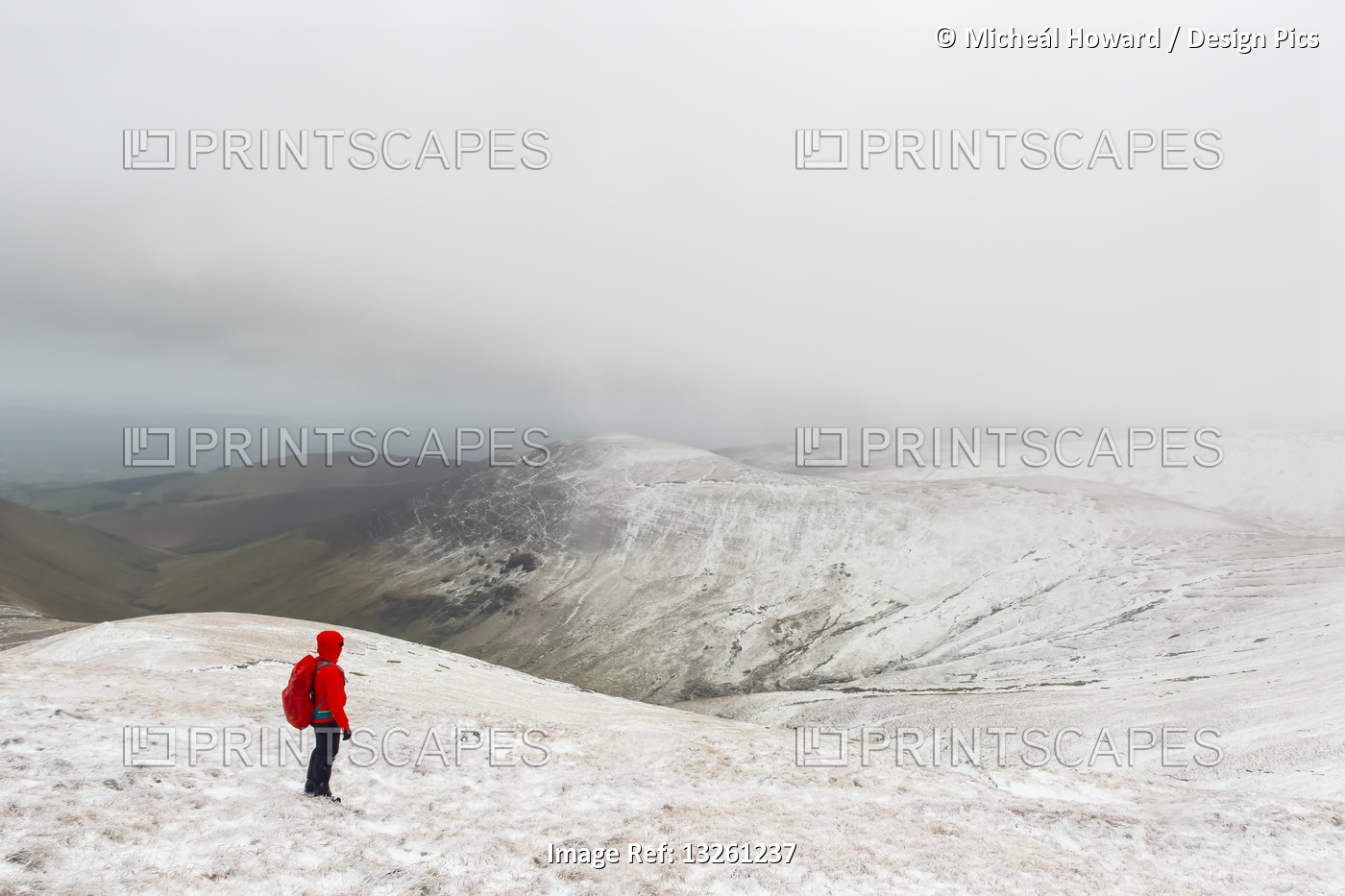 Female hiker in red jacket hiking on a snow-covered mountain in winter in bad ...