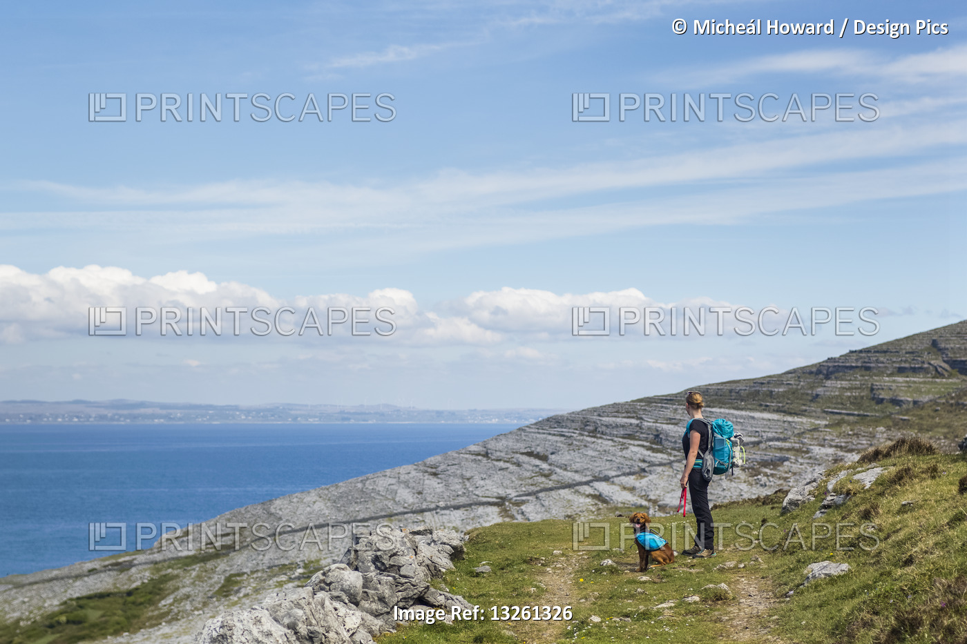 Woman and dog hiking on trail in the Burren looking out at the sea on a sunny ...