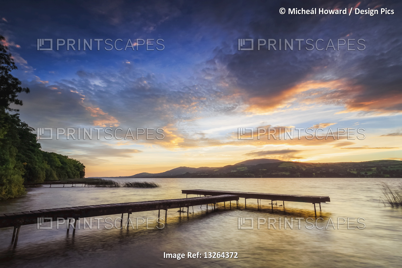 Dock on the bank of a lake with mountains in the background at sunrise; Two ...
