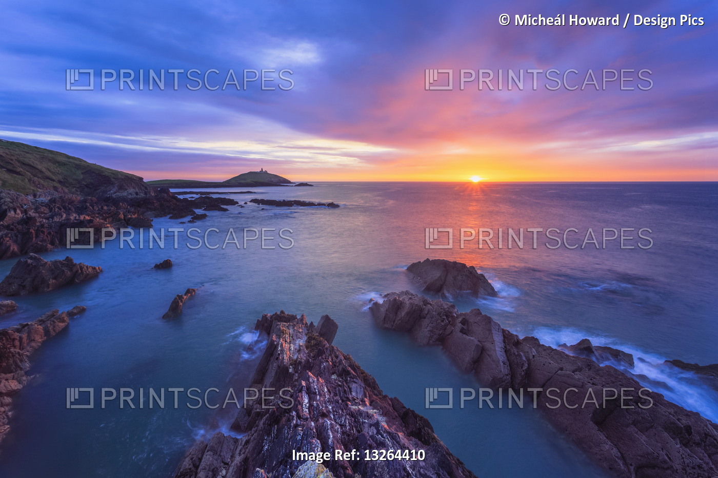 Sun rising over the Irish coastline with jagged rocks in the foreground and a ...