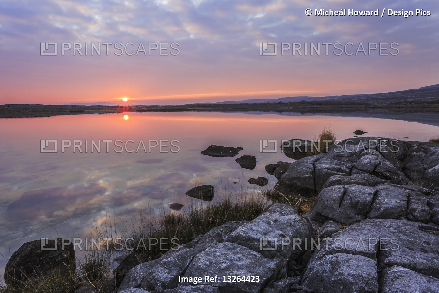 Sun setting over lake with reflections on a cloudy evening with limestone rocks ...