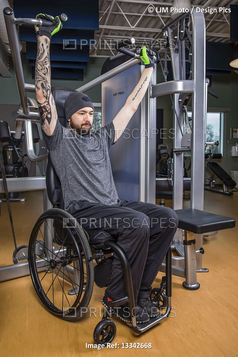 A paraplegic man working out using an overhead press in fitness facility; ...