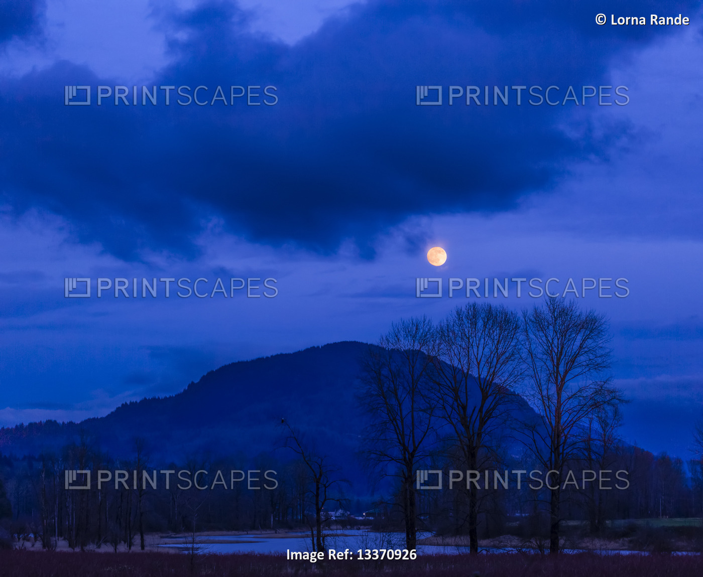 A glowing full moon in a cloudy sky over a silhouetted mountain, Village of ...