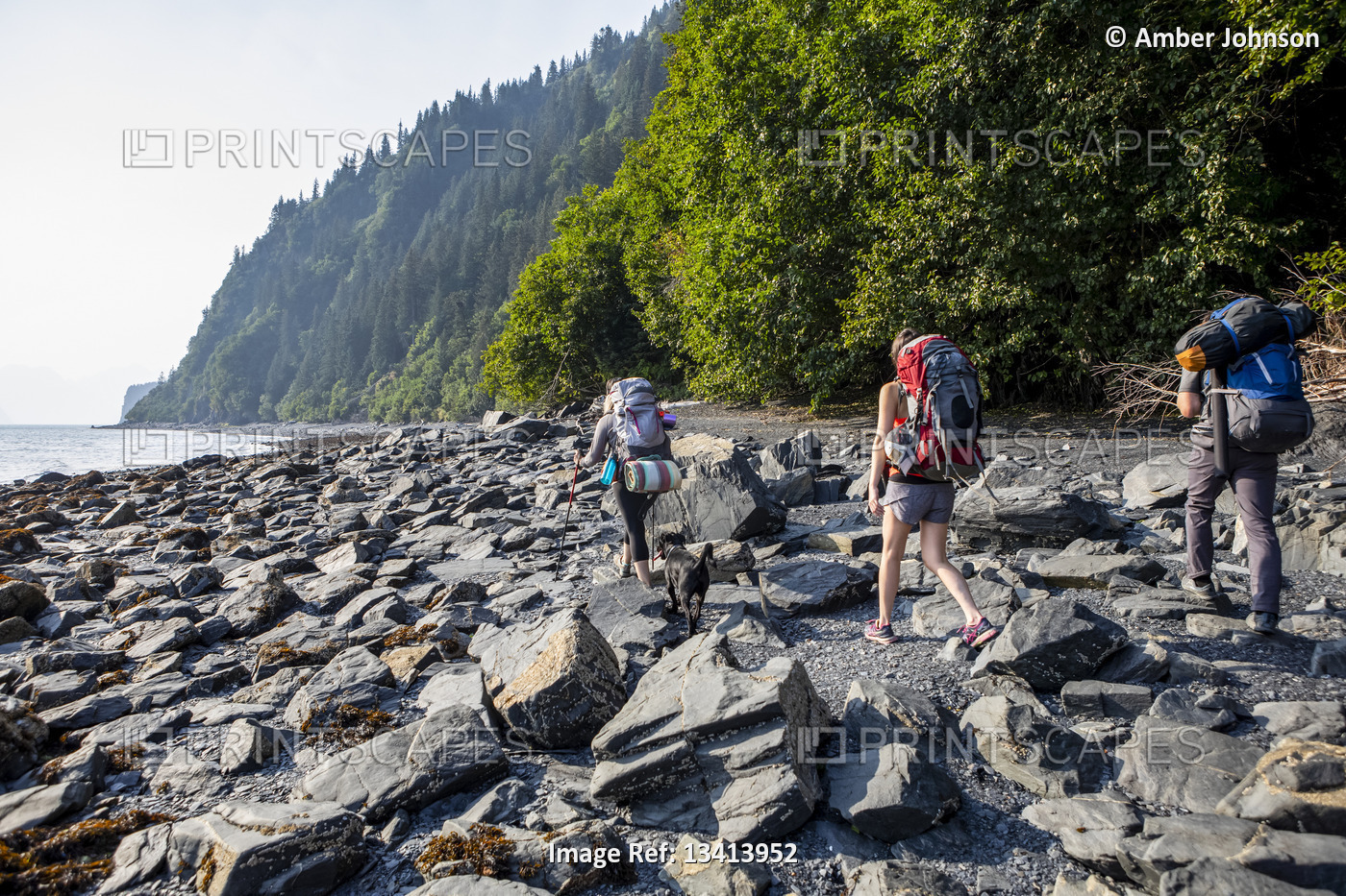 Millennials (one man, two women) backpacking on a rocky beach with their black ...