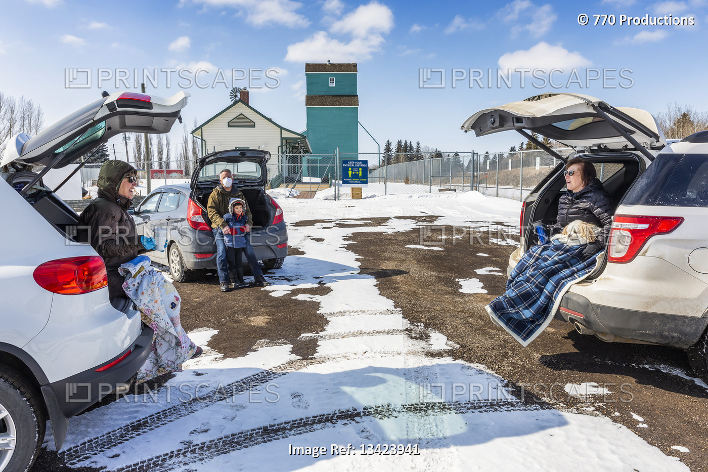 Families sit in the back of their vehicles in a parking lot to visit during the ...