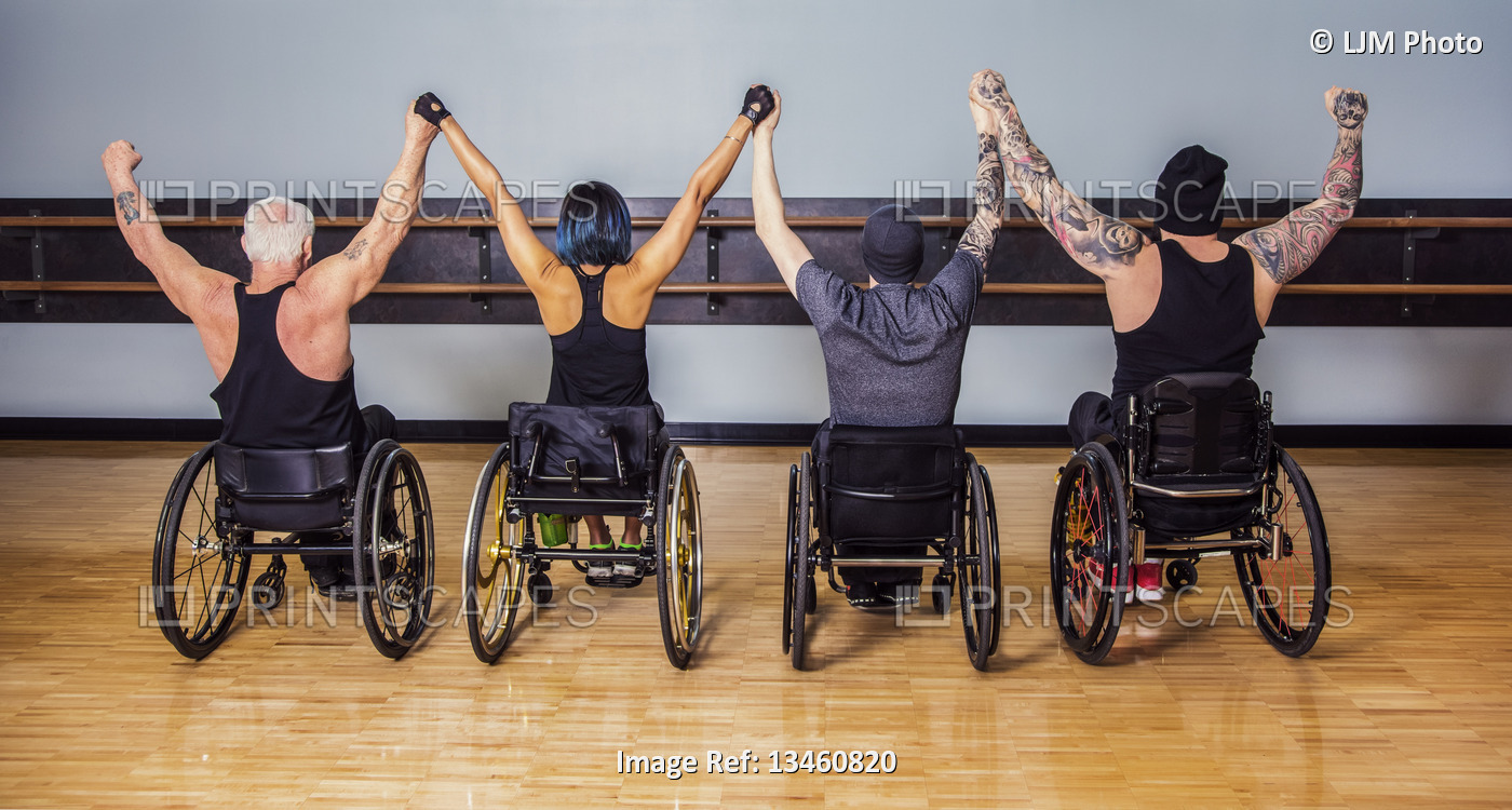 A view from behind of a group of paraplegic friends holding their hands high in ...