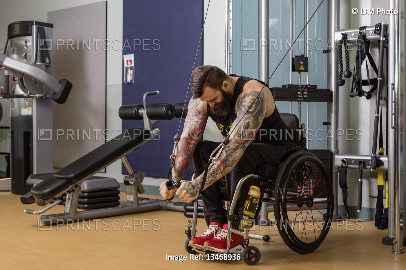 A paraplegic man working out using a crossover pulley weight lifting apparatus ...