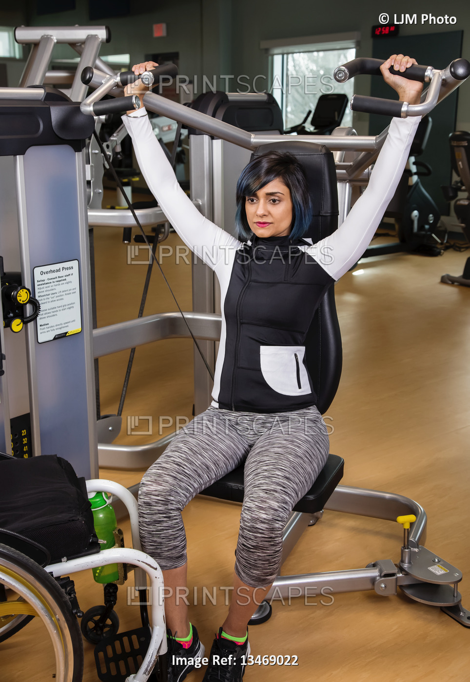 A paraplegic woman working out using an overhead press in a fitness facility; ...