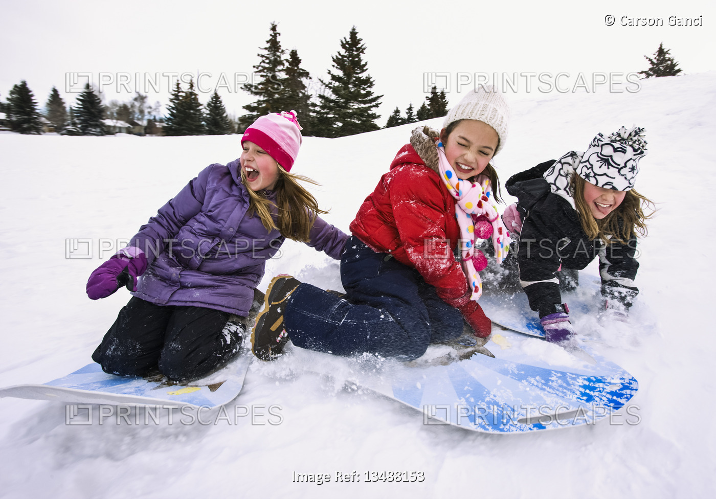 Three girls sledding downhill in the snow; Alberta, Canada