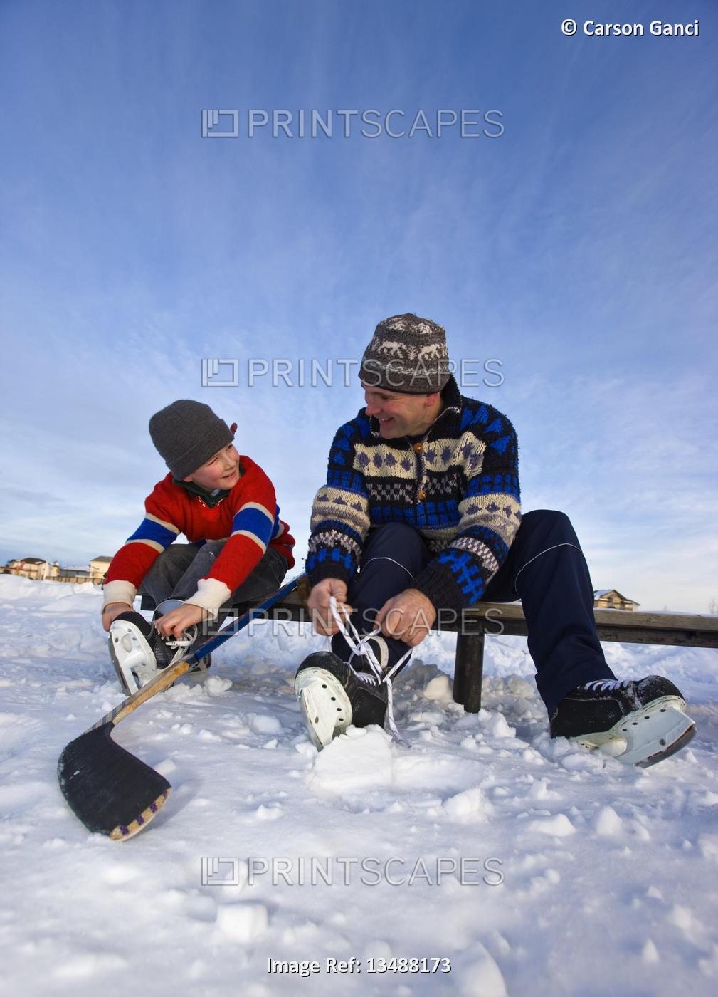 A father and son lacing their skates on a bench on a frozen lake for an outdoor ...