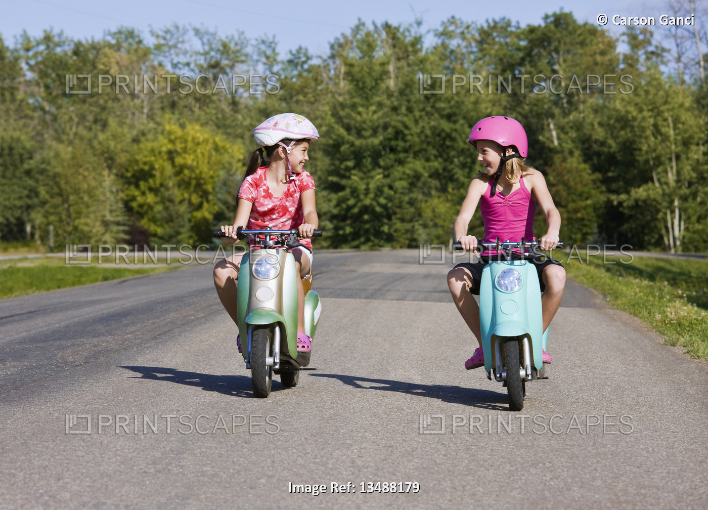 Two girls riding electric scooters down a paved country road; Canada