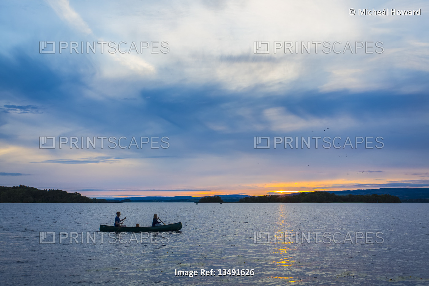 Man and woman paddling a canoe on Lough Derg lake at sunset; County Clare, ...