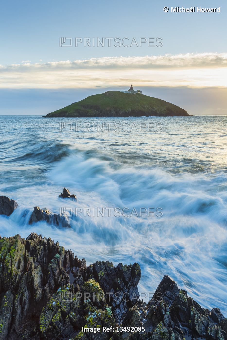 Waves crash against the coastal rocks with Ballycotton lighthouse in the ...