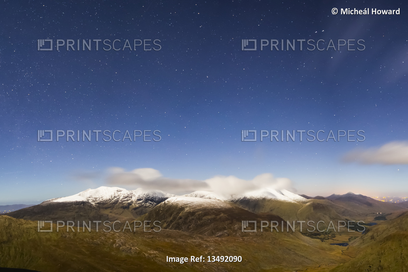 The MacGillycuddy's Reeks covered in snow at night with stars in the sky at ...