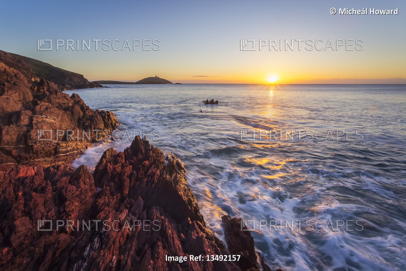 Sunrise over the Ballycotton cliffs with a lighthouse on an island on the ...
