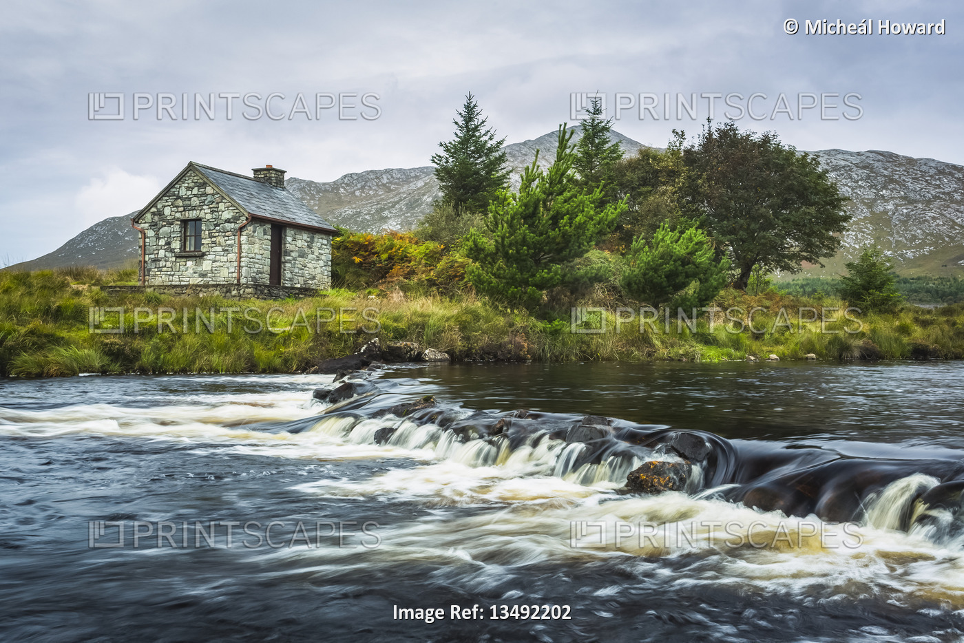 Small stone fisherman's hut on the banks of a small river with mountains in the ...