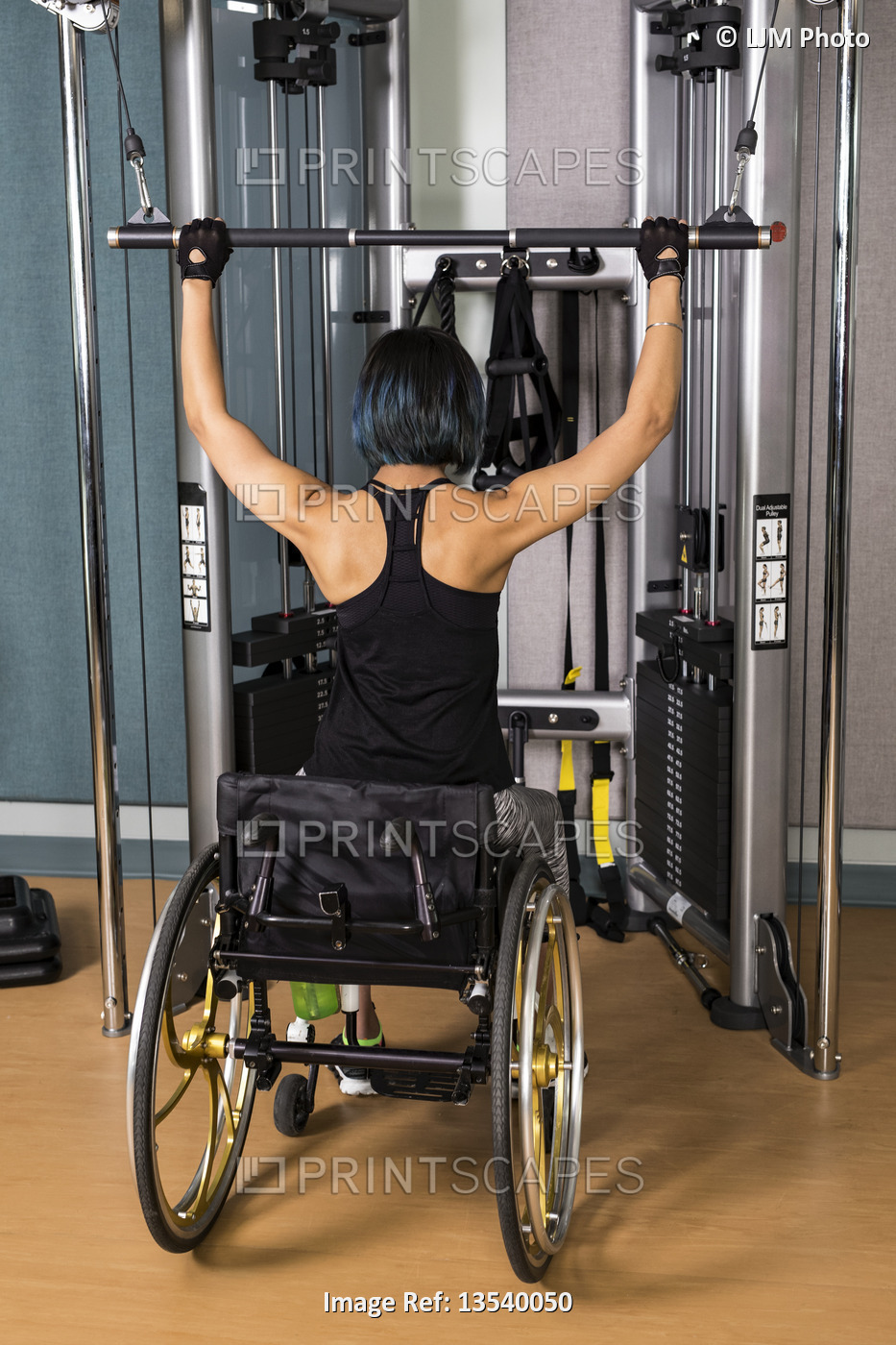 A view from behind of a paraplegic woman working out using a lat pull down ...