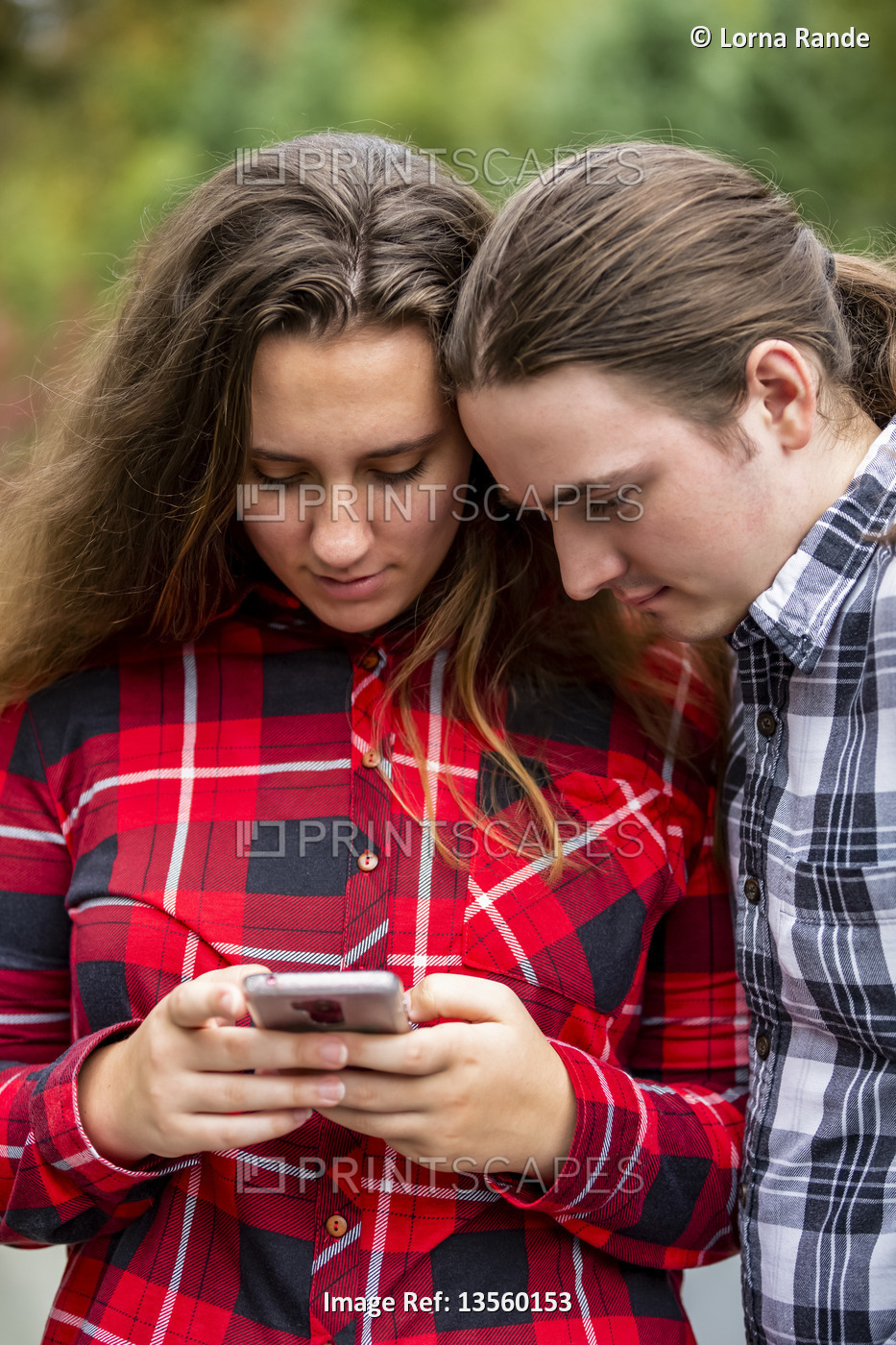 A young couple stands looking at a smart phone; Bothell, Washington, United ...