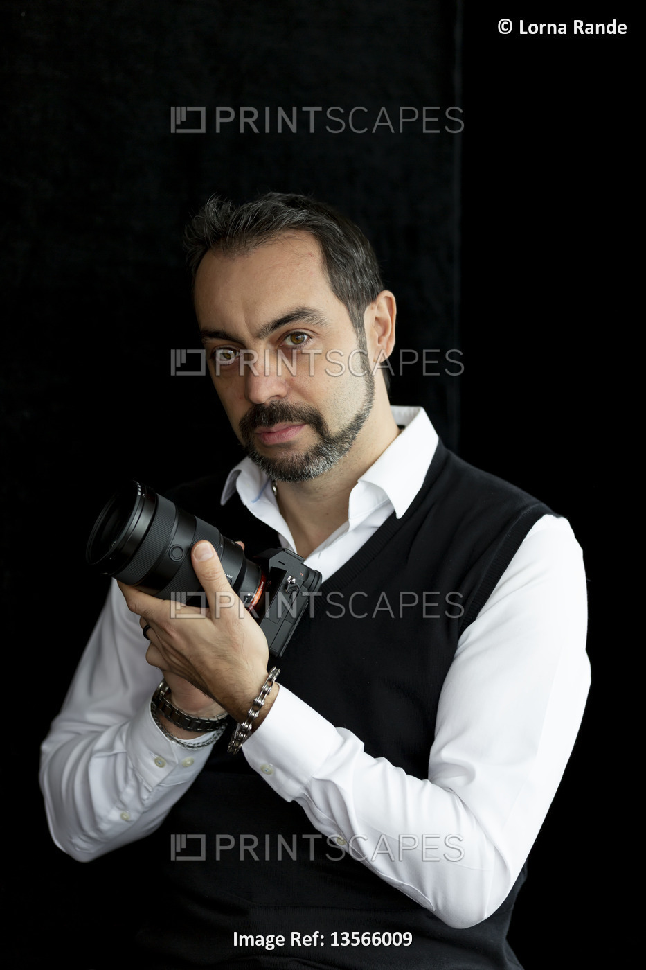 Portrait of a male photographer standing with his camera against a black ...