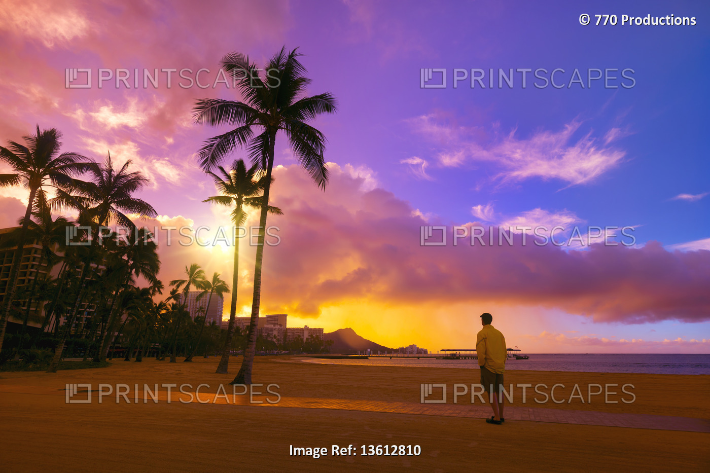A man stands on Waikiki Beach looking towards the condominiums and palm trees ...