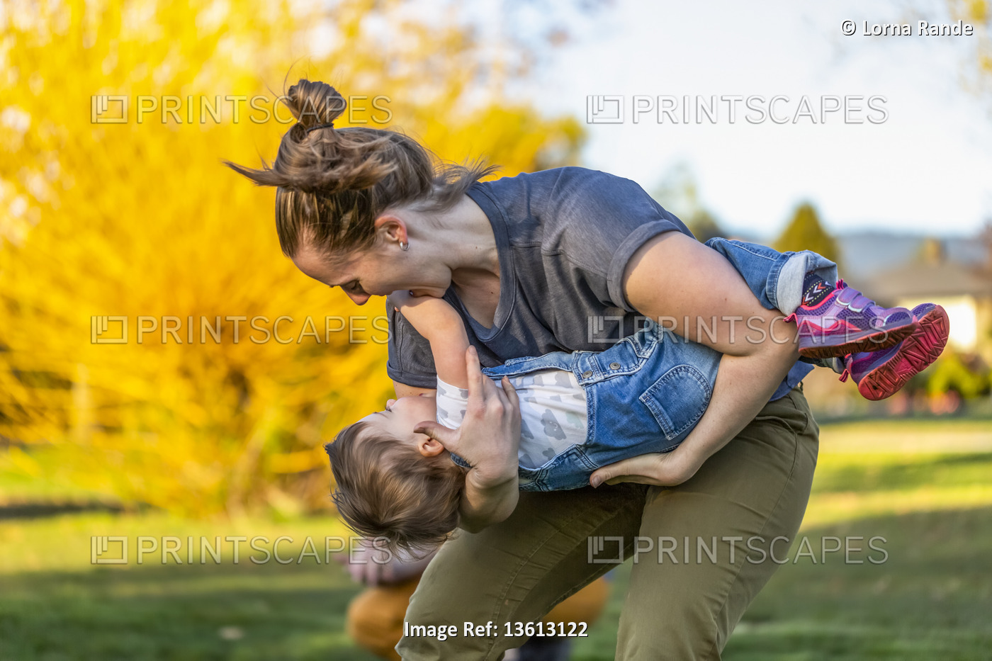 A mother plays with her toddler daughter in a park with autumn colours; North ...